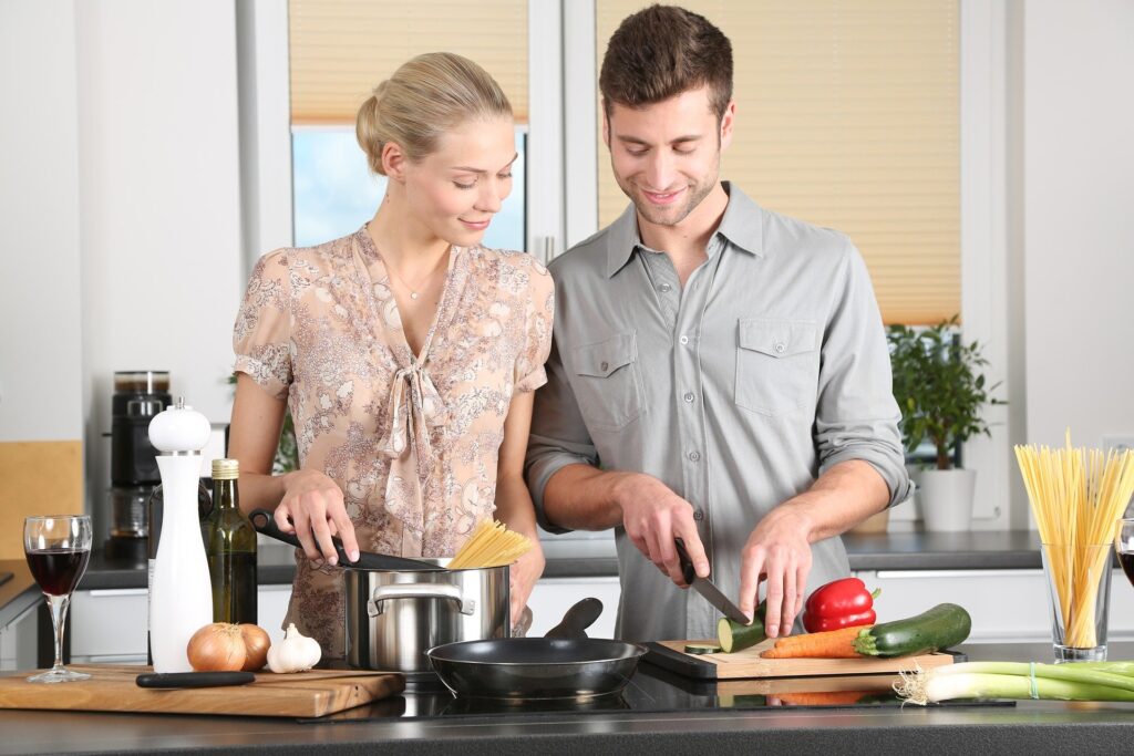 casal preparando uma refeição juntos diante da bancada da cozinha