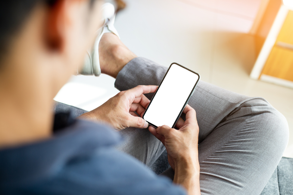 Homem sentado com a perna cruzada mexendo no celular