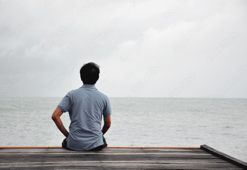 Homem sentado só em uma ponte de madeira olhando o mar
