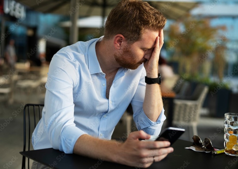 Homem vestido formal sentado em uma mesa mexendo no celular preocupado