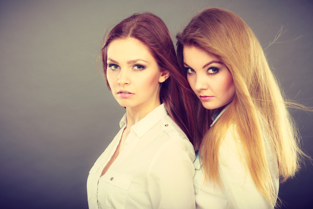 Duas mulheres uma loira e outra morena vestidas de blusa social fazendo pose