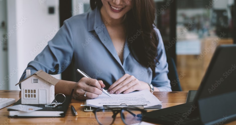 Mulher vestida de forma formal escrevendo em um caderno sobre uma mesa