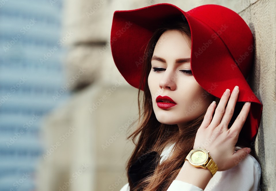 Mulher com batom e chapéu vermelho com relógio dourado no braço