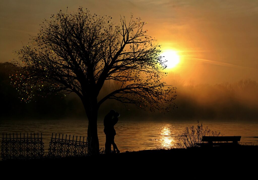 casal se beijando ao pôr do sol em frente a lago