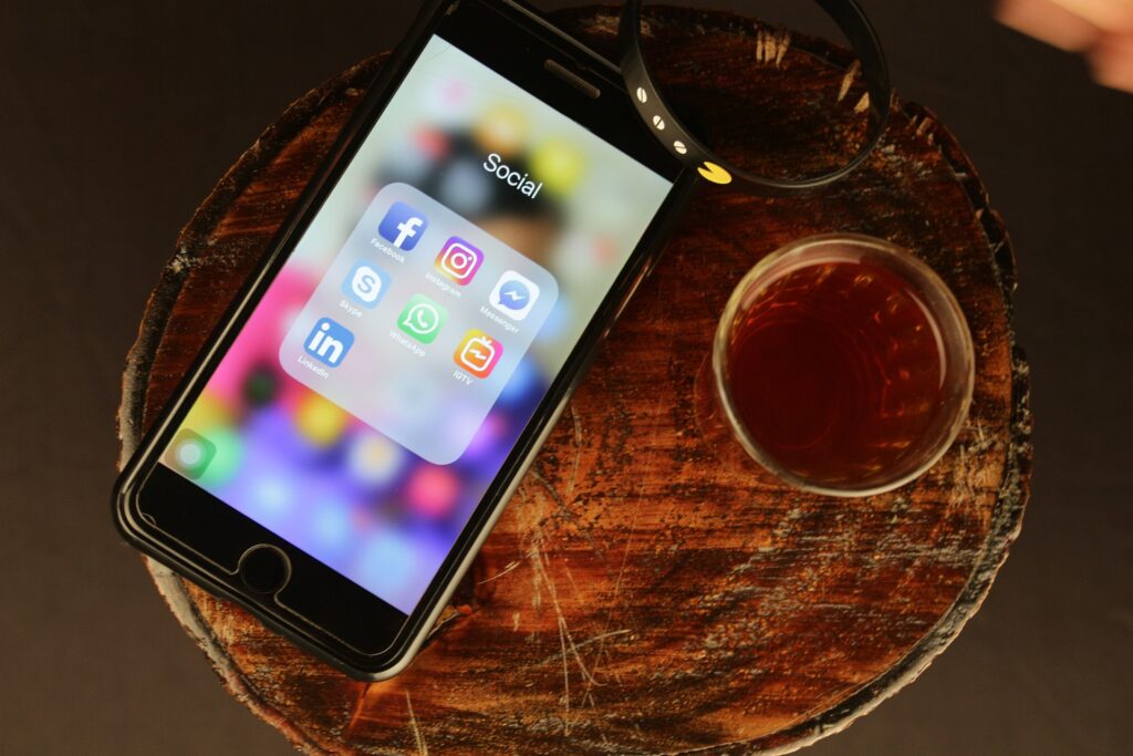 celular em cima de uma mesa, ao lado de uma xícara de chá, com tela ligado exibindo os botões das principais redes sociais
