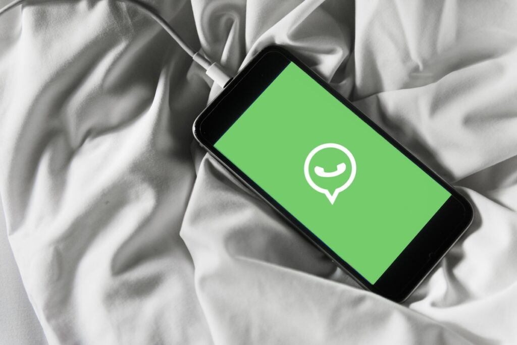 celular carregando em cima da cama e iniciando o aplicativo whatsapp