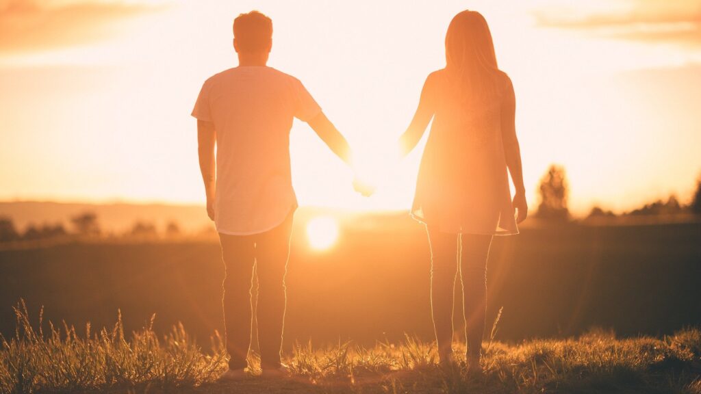 casal de mãos dadas assistindo o pôr do sol em uma colina