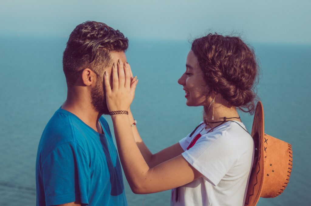 mulher com as mãos sobre o rosto de homem em um passeio ao ar livre. Ela sorri, ele está a vontade