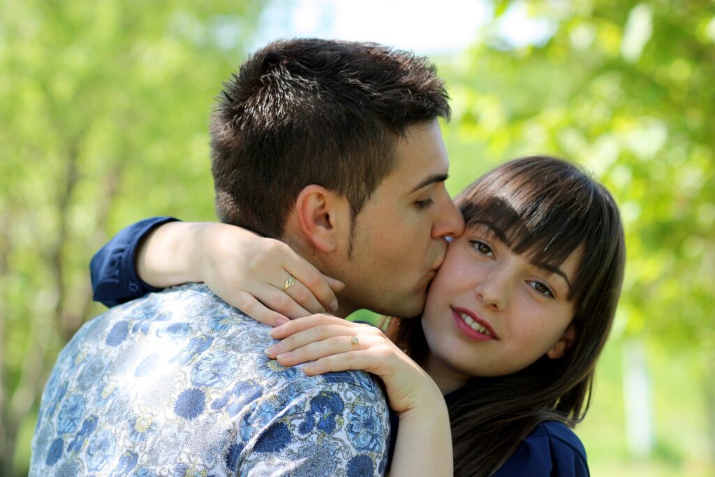 homem beija sua companheira no rosto enquanto ela olha para câmera