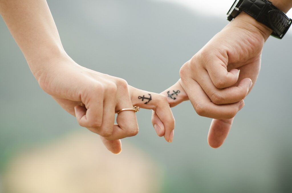 mãos de casal engatadas com tatuagens iguais e anel