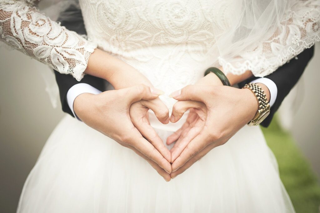 casal de noivos abraçados, com o noivo atrás da noiva, ambos fazendo um coração com as mãos juntas sobre a barriga da noiva