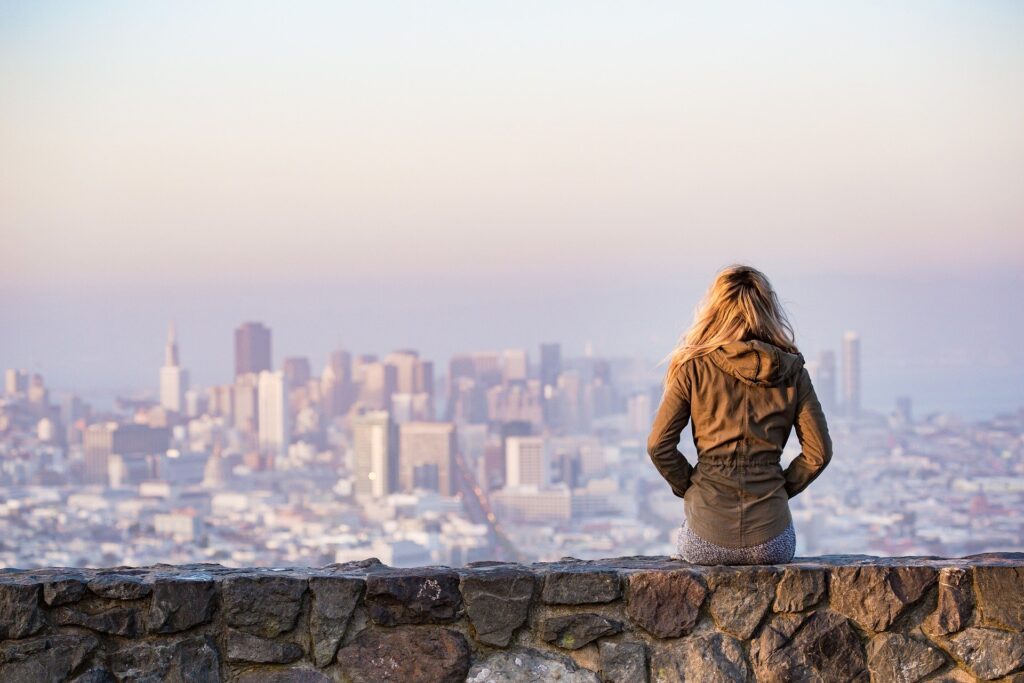mulher sentada sobre muro olhando a cidade e o horizonte