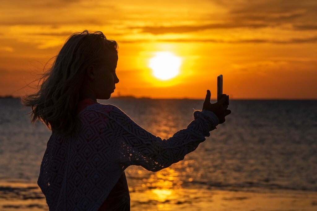 mulher tirando uma selfie na praia ao pôr do sol