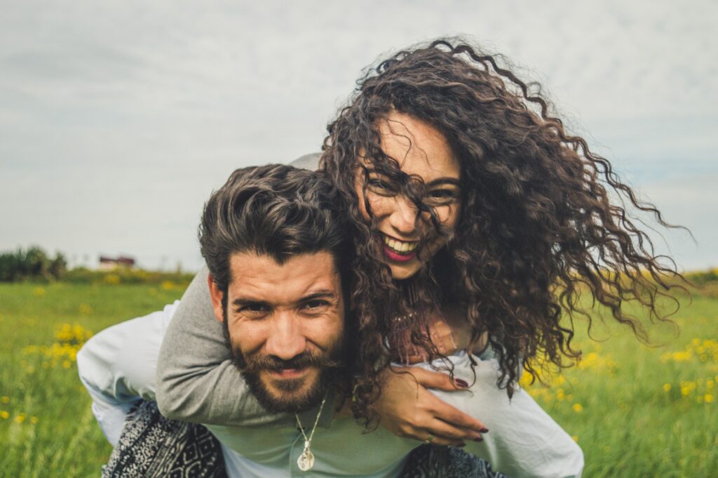 homem carrega mulher nas costas e ambos sorriem no campo