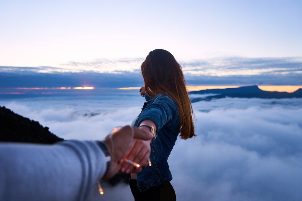 mulher segura a mão do companheiro enquanto aprecia a vista do alto de uma montanha