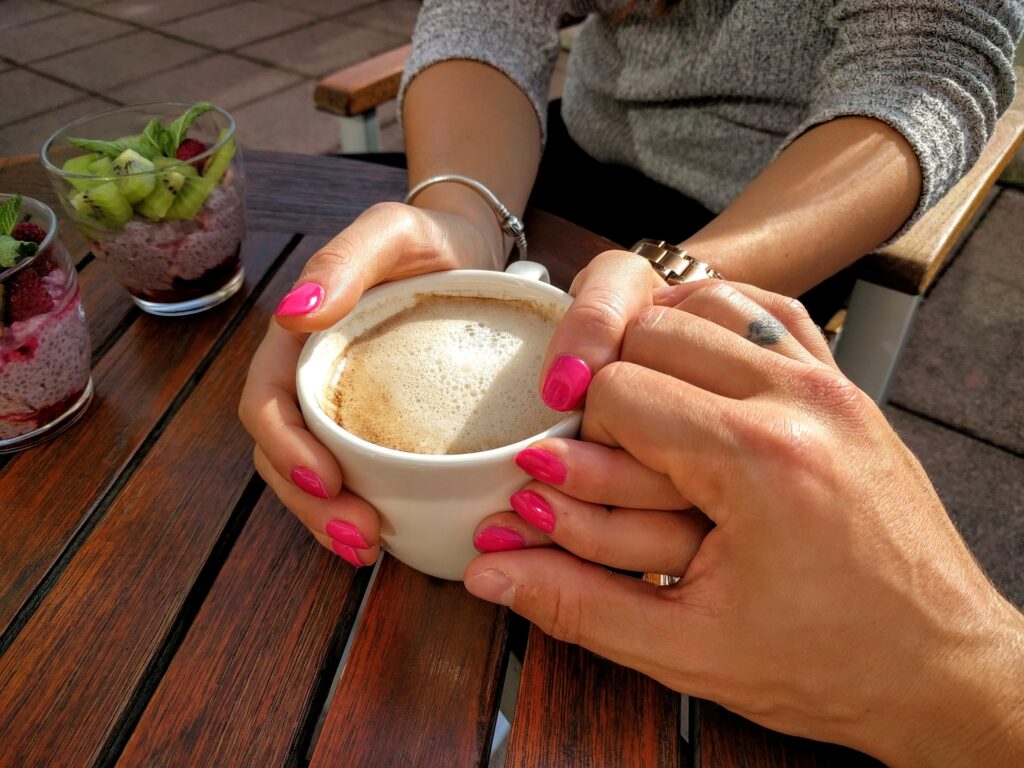 homem segura mão de mulher enquanto ela segura uma xícara de café sobre a mesa