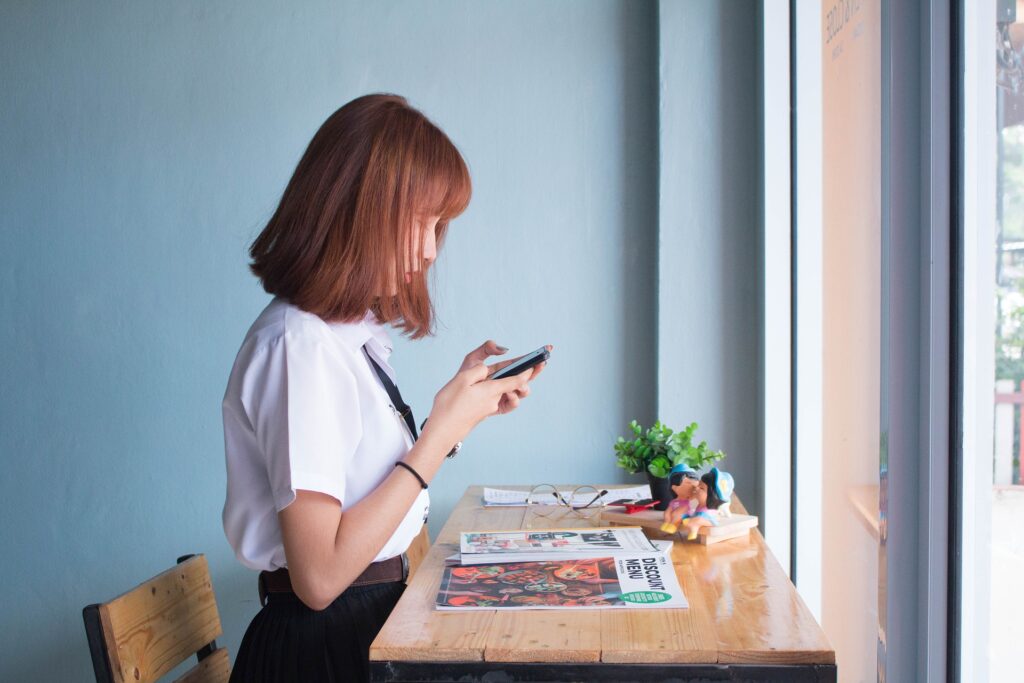 mulher sentada em frente a uma mesa na sala e fazendo uma publicação com o celular