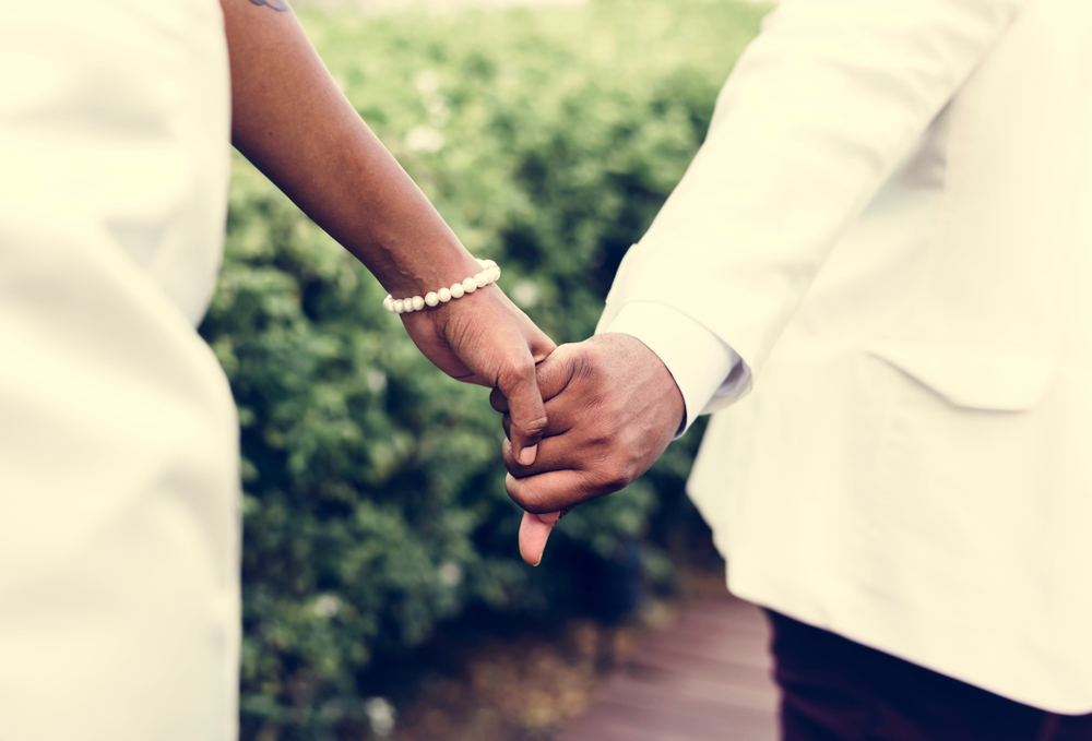 foto exige close sobre as mãos dadas de um casal. Homem de terno segura a mão da esposa em vestido de festa