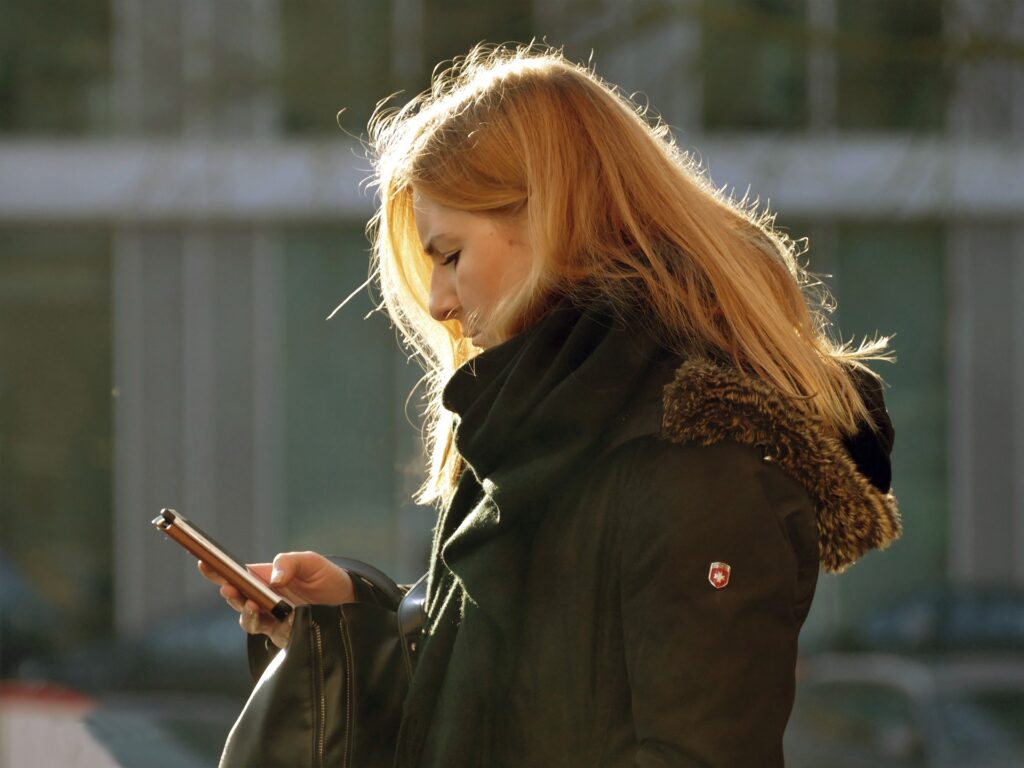 mulher usando o celular na rua e vestindo roupas de frio