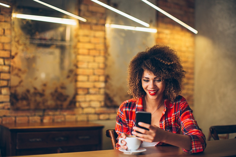 mulher em um bar recebe mensagem no celular enquanto toma café e sorri