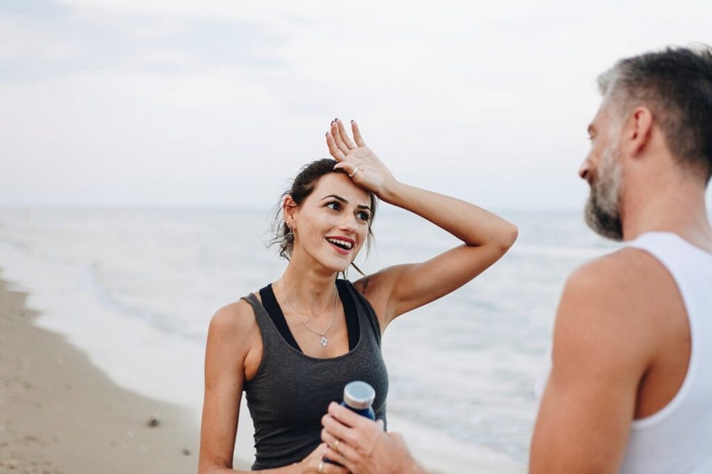 mulher correndo na praia fala com homem que lhe oferece água
