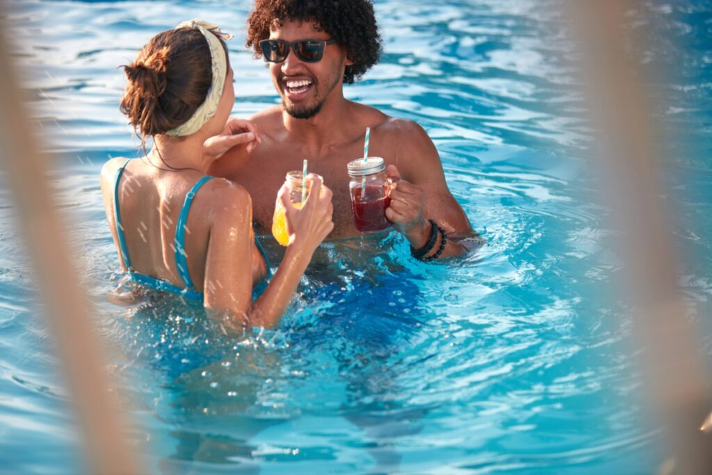 casal em piscina com drinks na mão e conversando com proximidade