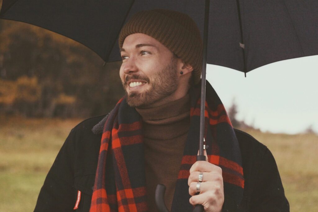 homem em roupas de frio segura guarda chuva em dia chuvoso no campo