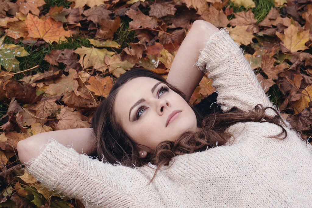 mulhr deitada sobre folhas de outono olha para cima pensativa
